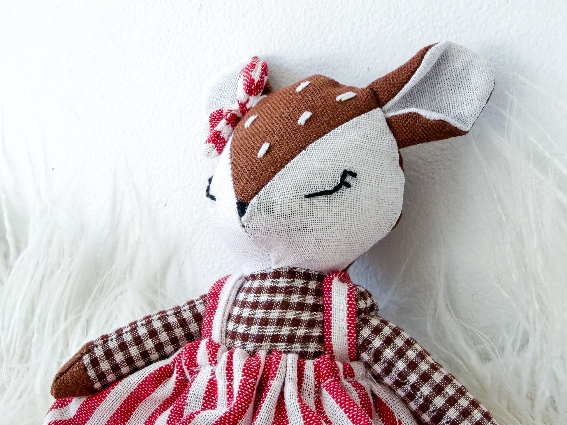 Stuffed deer toy with a red and white striped dress on a fluffy white surface