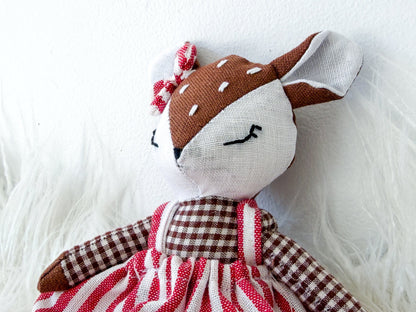 Stuffed deer toy with a red and white striped dress on a fluffy white surface
